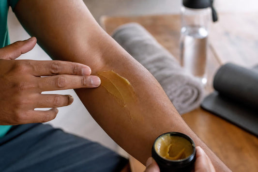 Application d’un baume chinois sur l’avant-bras avant/après effort, scène réaliste avec texture du baume et ambiance naturelle sur table en bois.